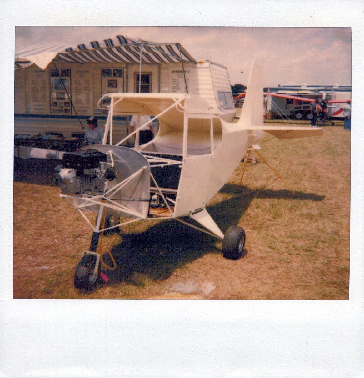 Instant photograph of an uncovered Carlson Sparrow fuselage with engine installed, on display outdoors
