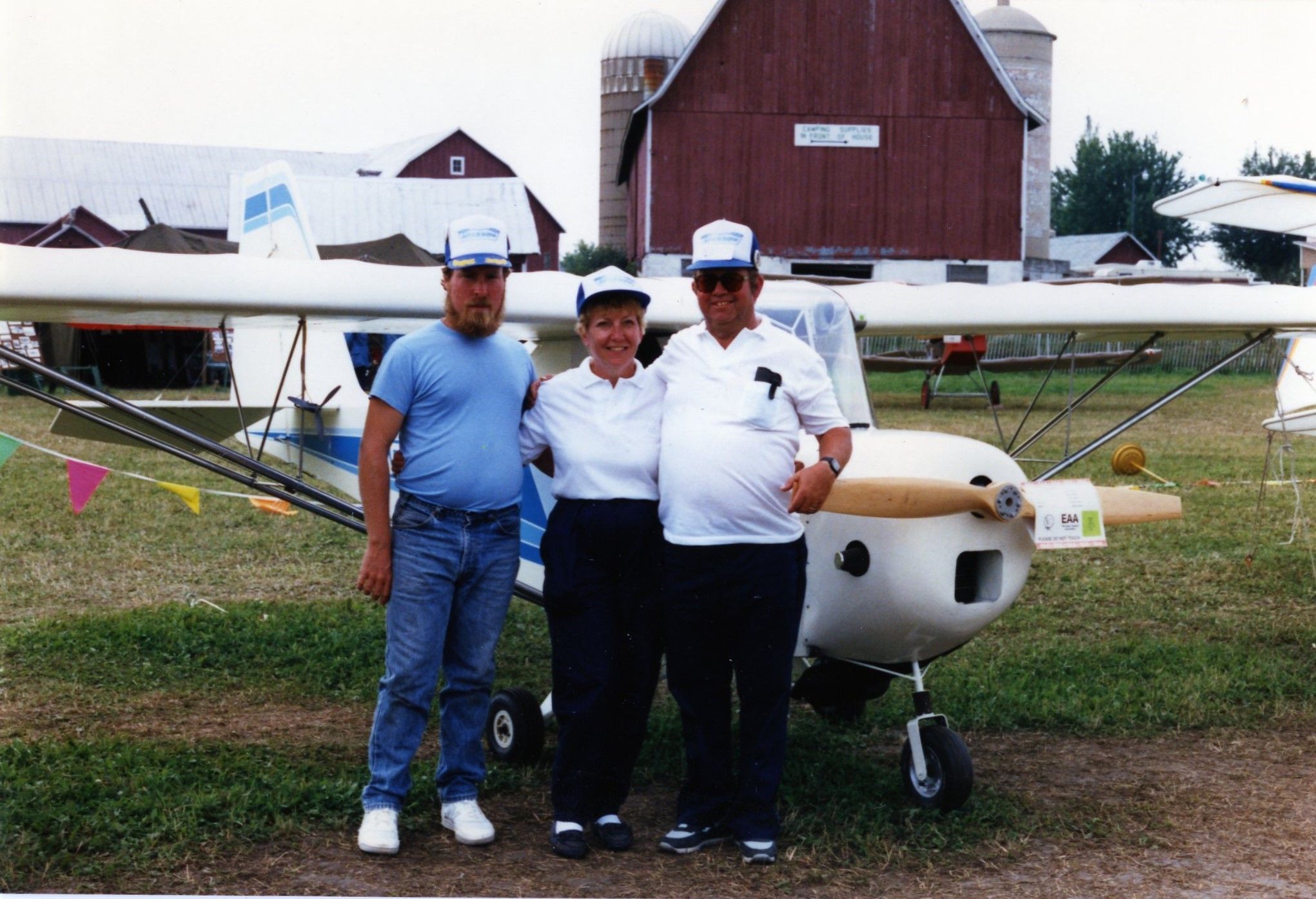 Three people in caps standing in front of a Carlson Sparrow at a fly-in