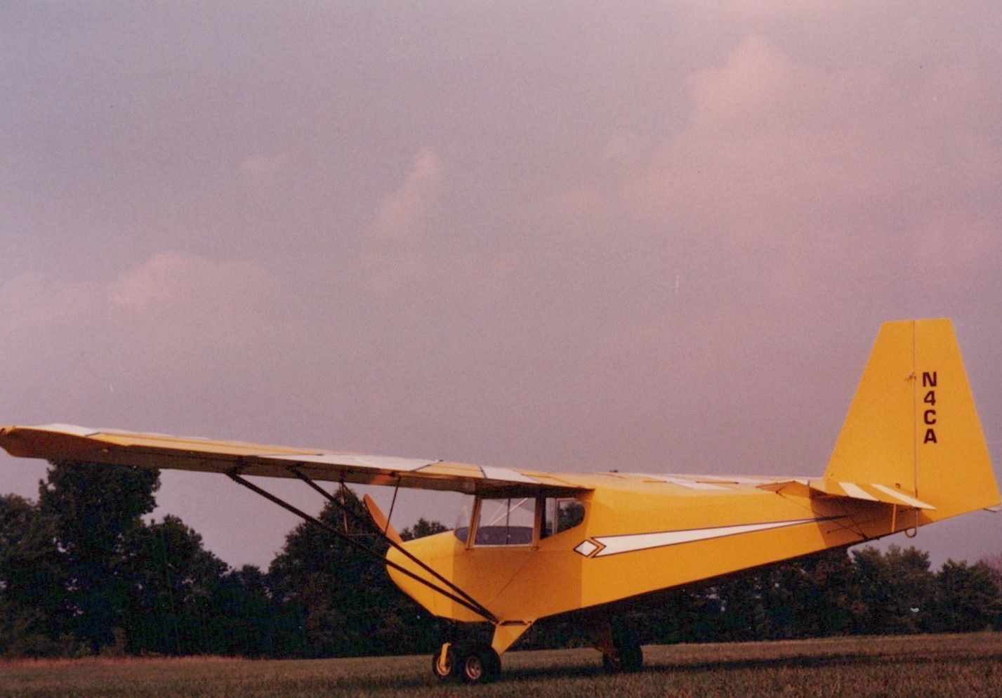 Yellow Carlson Sparrow II XTC parked at the edge of a field in evening light