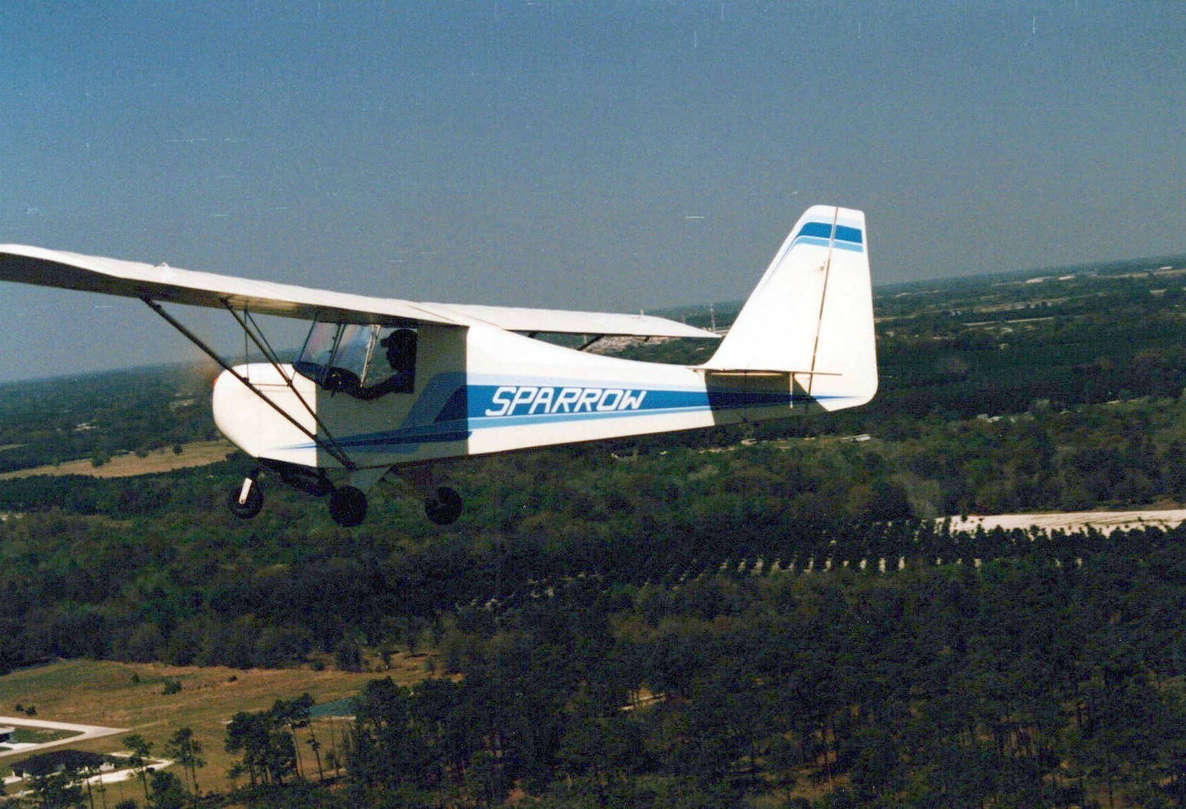 Carlson Sparrow Ultralight in flight over a tree line