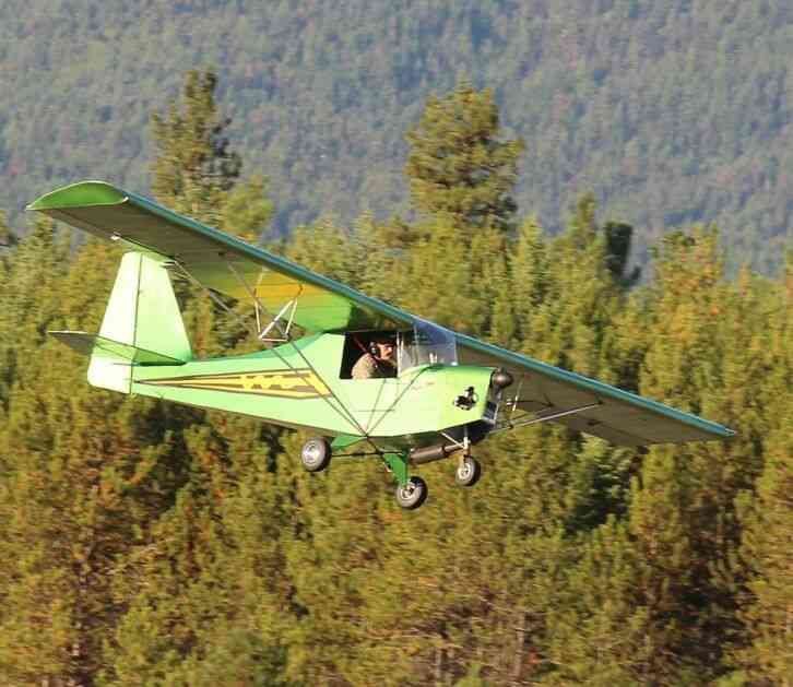 Green Carlson Sparrow Ultralight flying low over evergreen trees