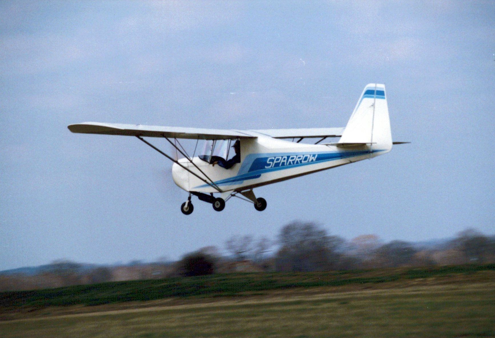 Carlson Sparrow Ultralight making a low pass against a blue sky