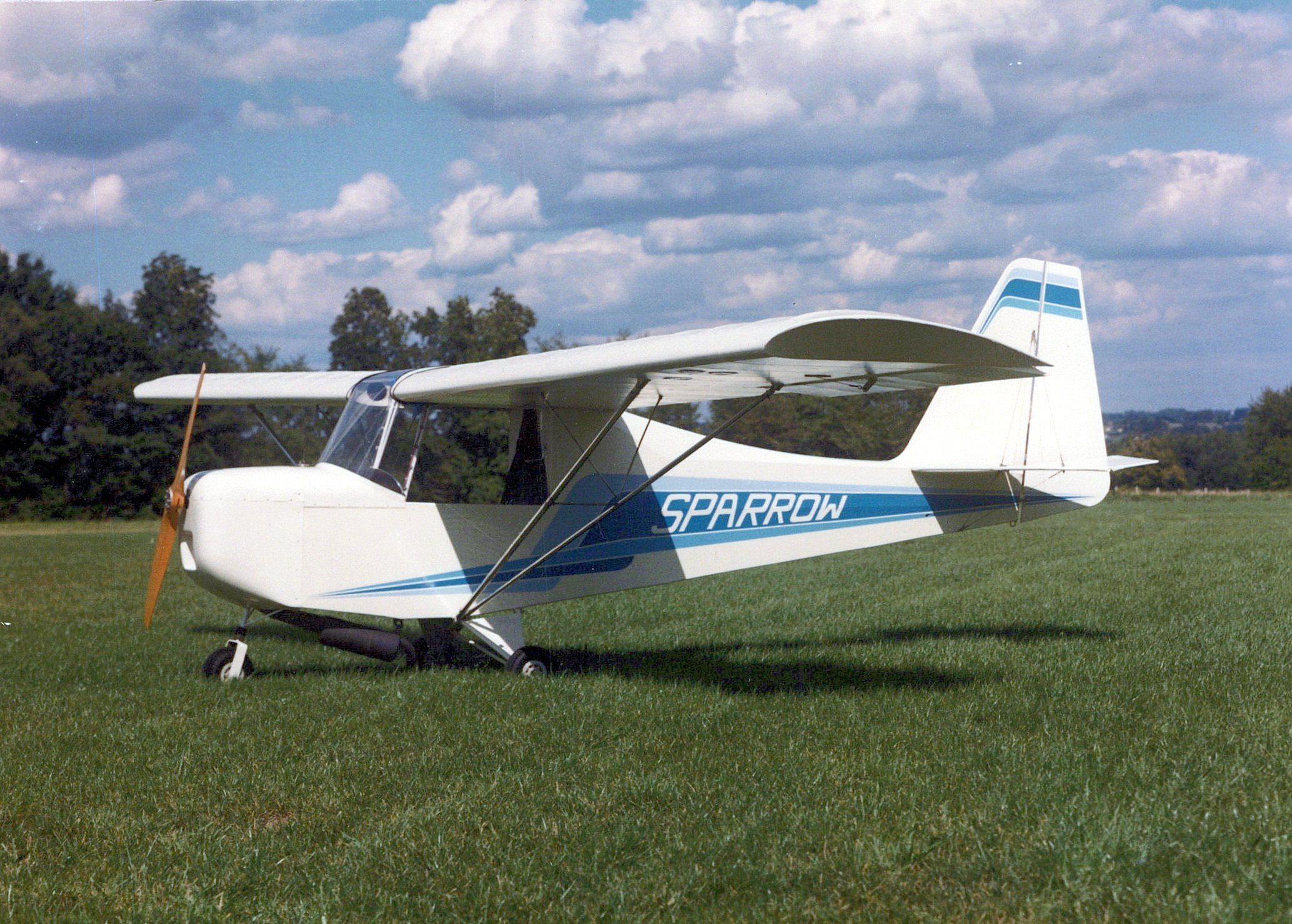 White and blue Carlson Sparrow Ultralight parked on a grass field